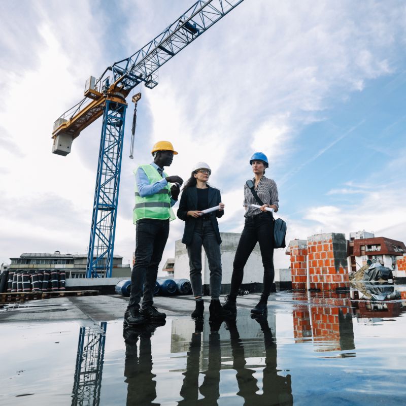 Three workers with hardhats in front of a crane